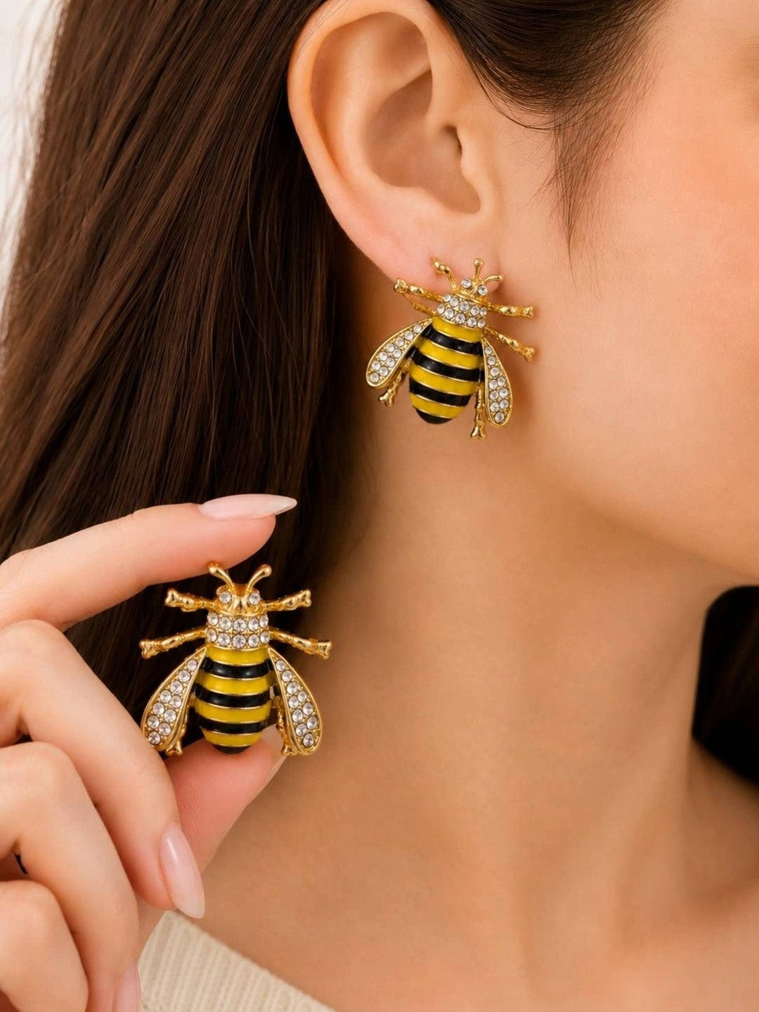 Woman wearing gold bee stud earring on ear while holding the second earring between fingers