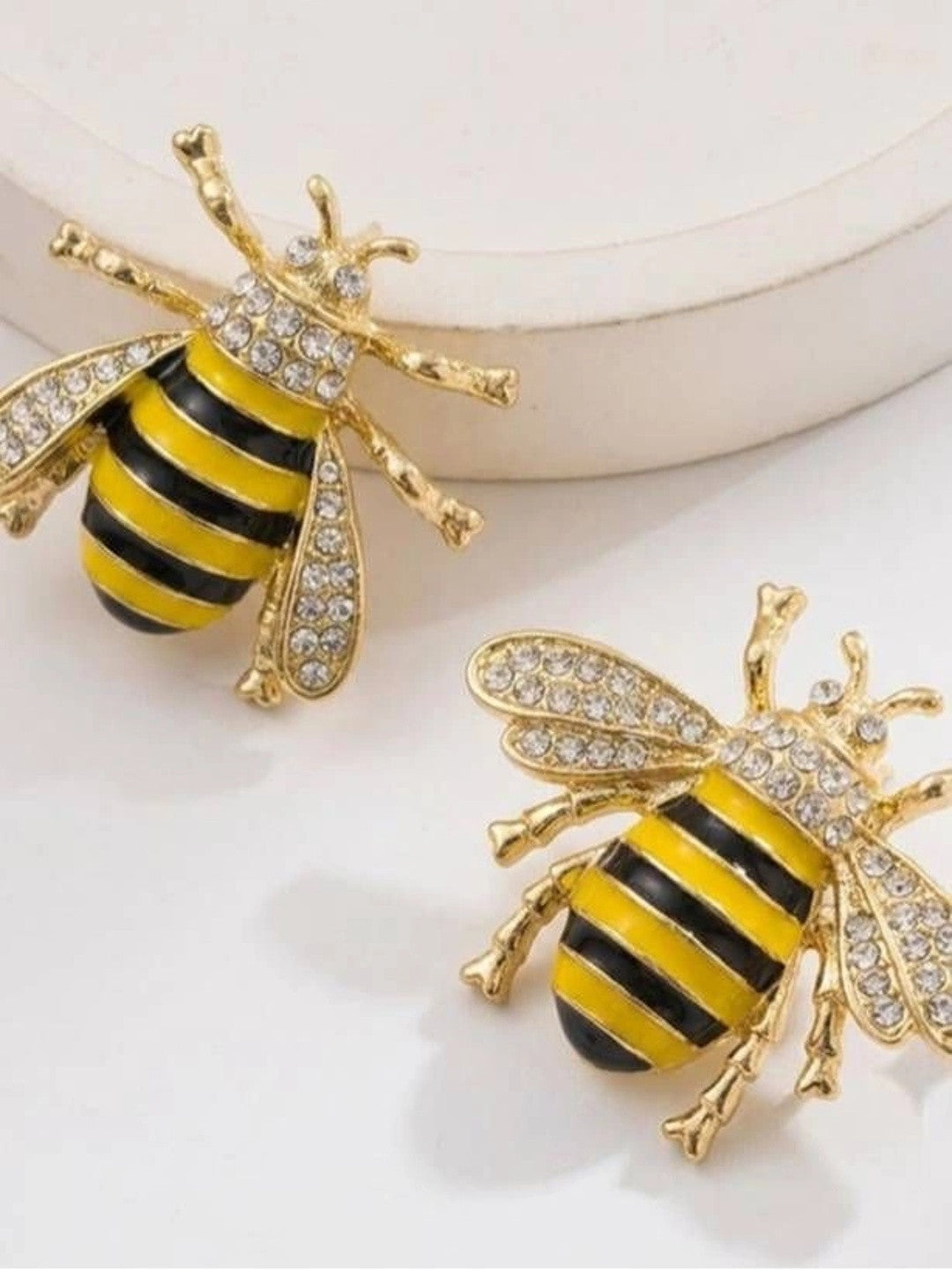 Two gold bee stud earrings with crystal embellished wings and enamel striped abdomen on white surface