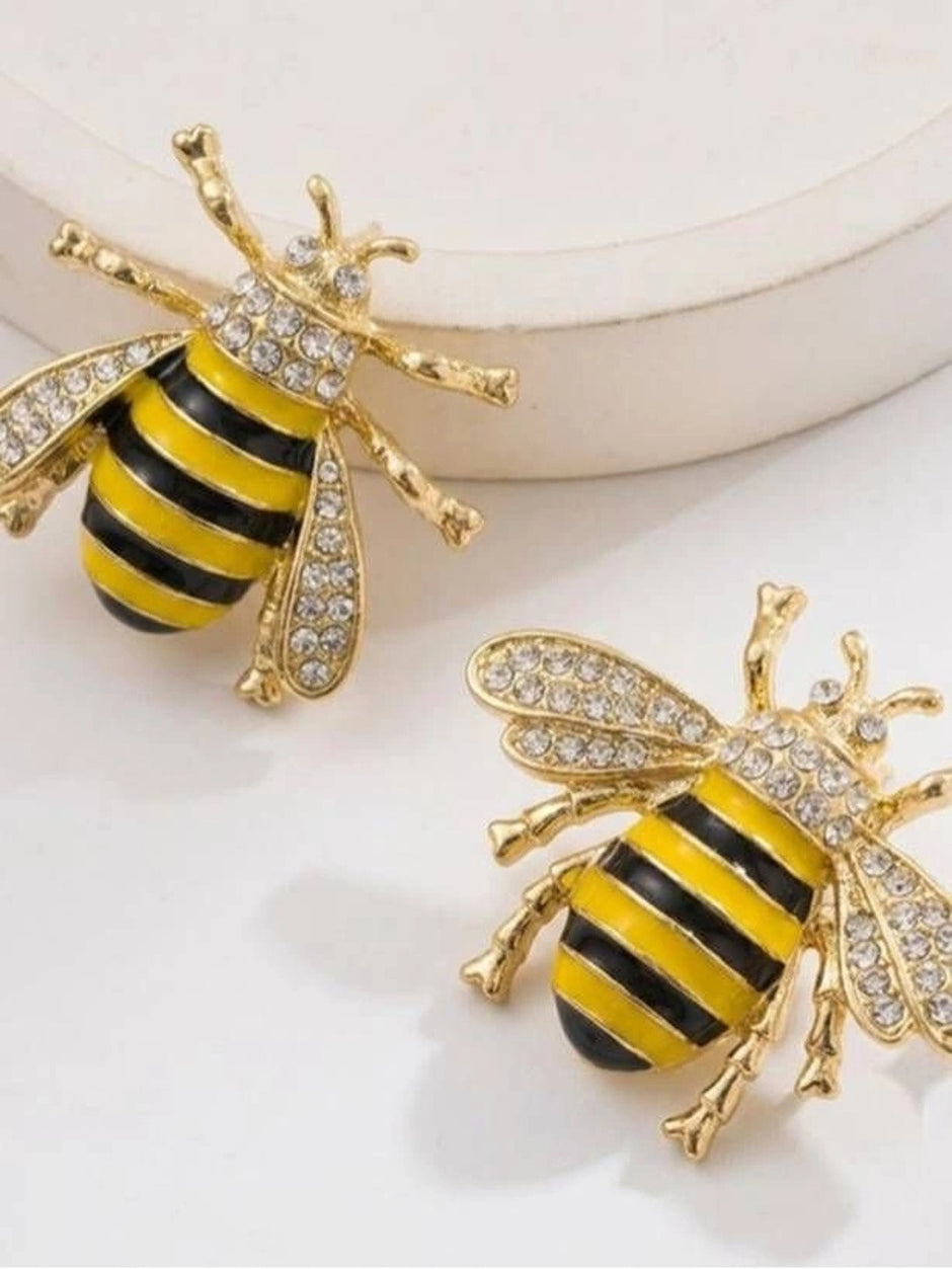 Two gold bee stud earrings with crystal embellished wings and enamel striped abdomen on white surface