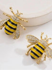 Two gold bee stud earrings with crystal embellished wings and enamel striped abdomen on white surface