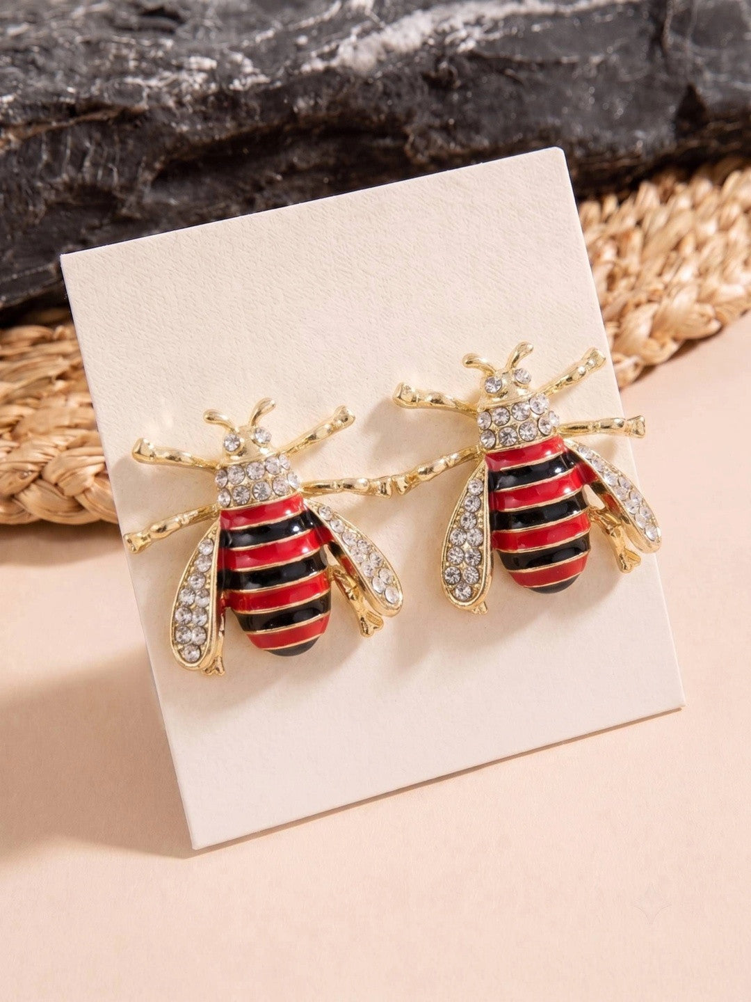 Pair of gold-tone bee stud earrings with red black enamel stripes and crystal wings displayed on white jewellery card