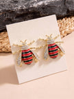 Pair of gold-tone bee stud earrings with red black enamel stripes and crystal wings displayed on white jewellery card
