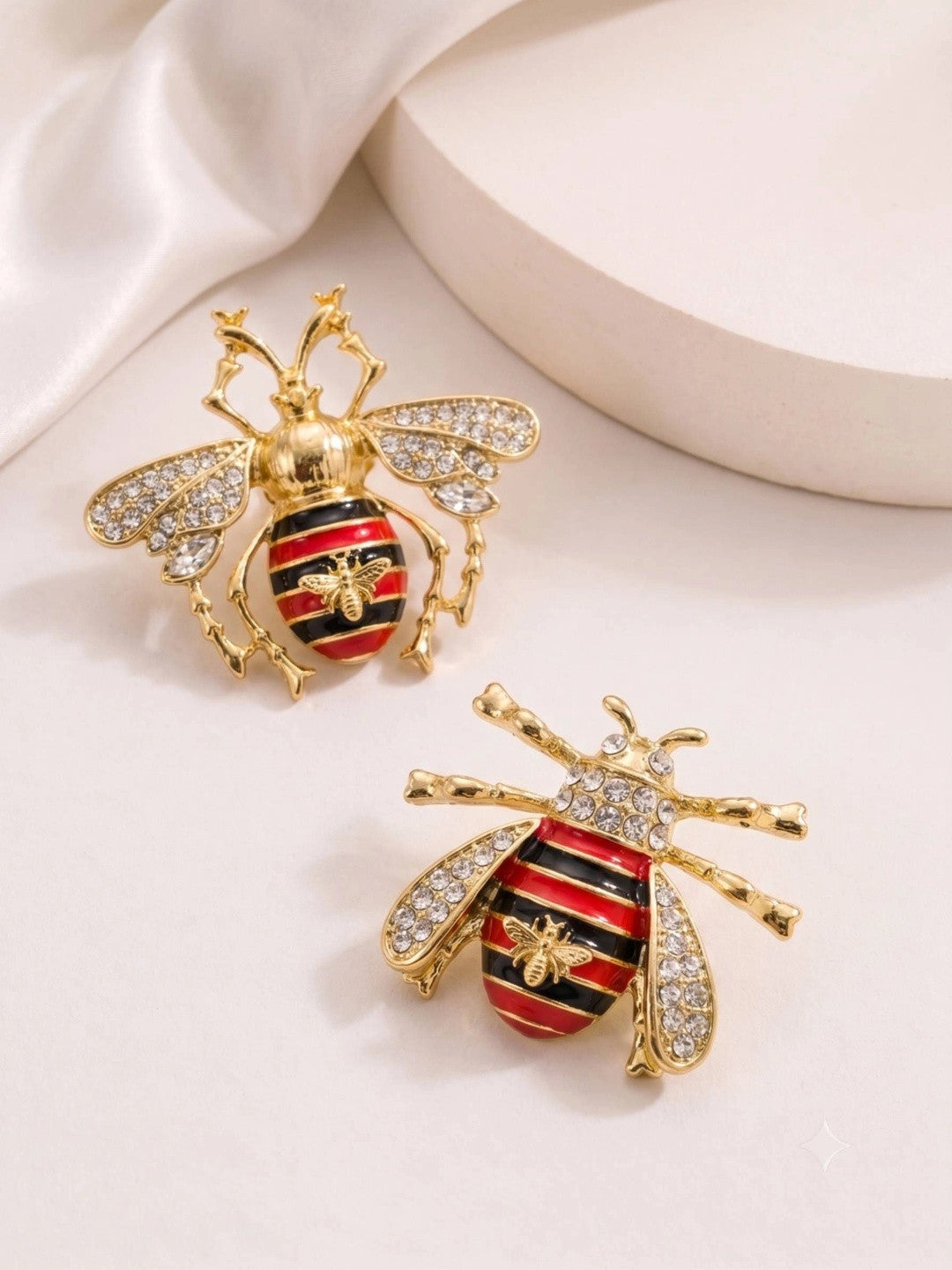 Two gold bee earrings with enamel striped abdomen and crystal wings laid flat on white surface