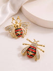 Two gold bee earrings with enamel striped abdomen and crystal wings laid flat on white surface