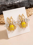 Gold bee stud earrings with yellow enamel body displayed on a white jewellery card against a textured background