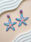 Both raffia starfish earrings laid flat on a peach surface beside a white sculptural prop showing full design detail