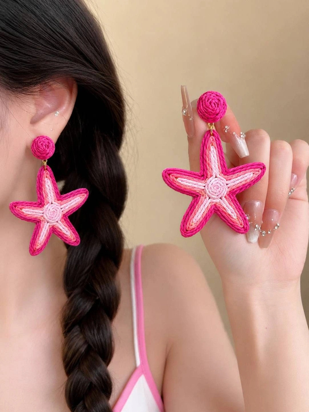 Woman wearing hot pink raffia starfish drop earrings with a braided hairstyle and pink outfit