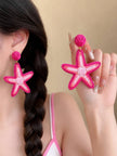 Woman wearing hot pink raffia starfish drop earrings with a braided hairstyle and pink outfit