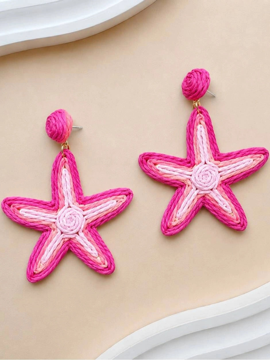 Pair of pink raffia woven starfish drop earrings laid flat on a beige surface