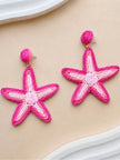 Pair of pink raffia woven starfish drop earrings laid flat on a beige surface
