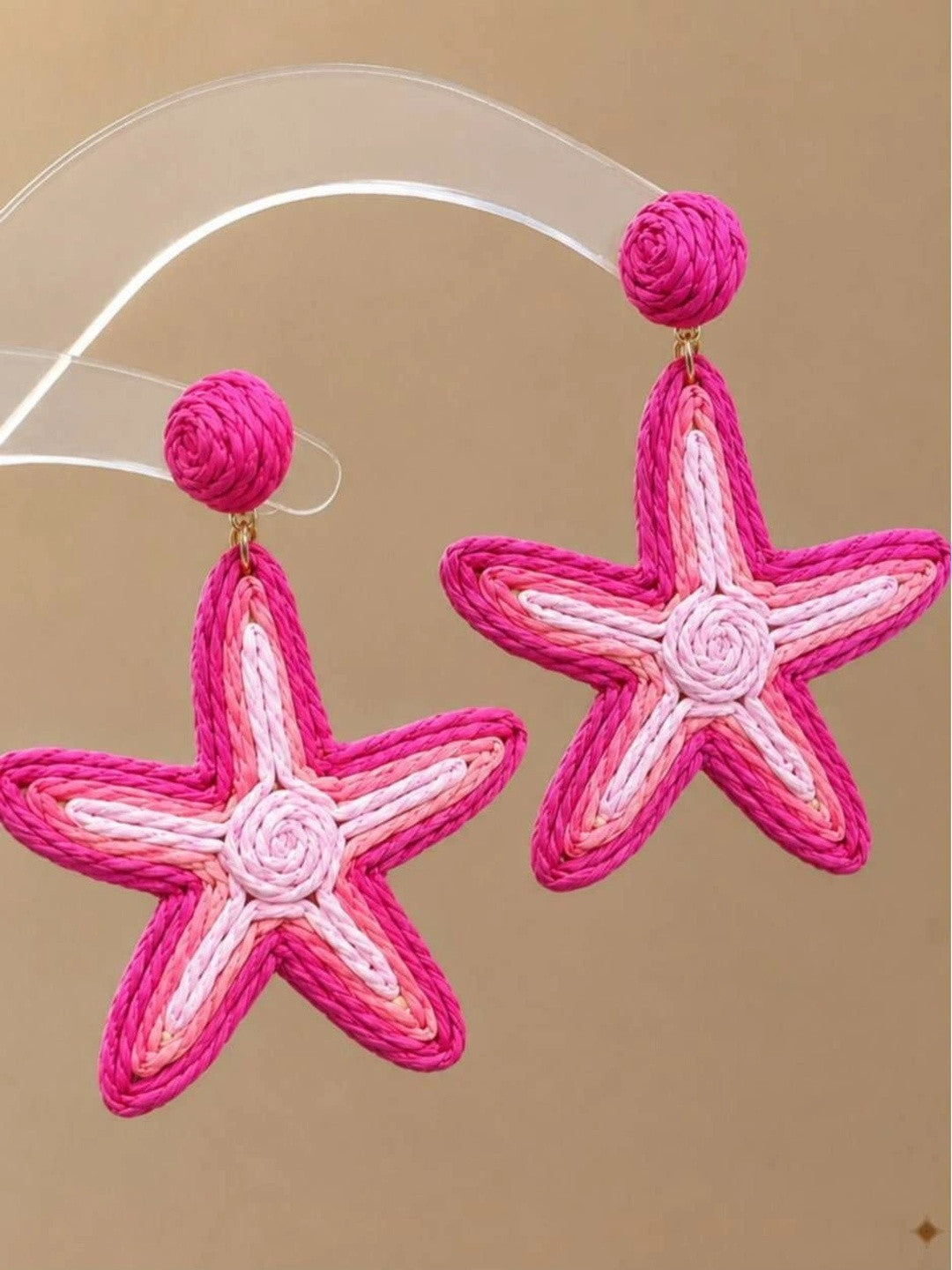 Close-up of two pink raffia starfish drop earrings suspended against a neutral background