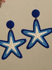 Pair of blue and cream raffia woven starfish drop earrings hanging against a neutral background