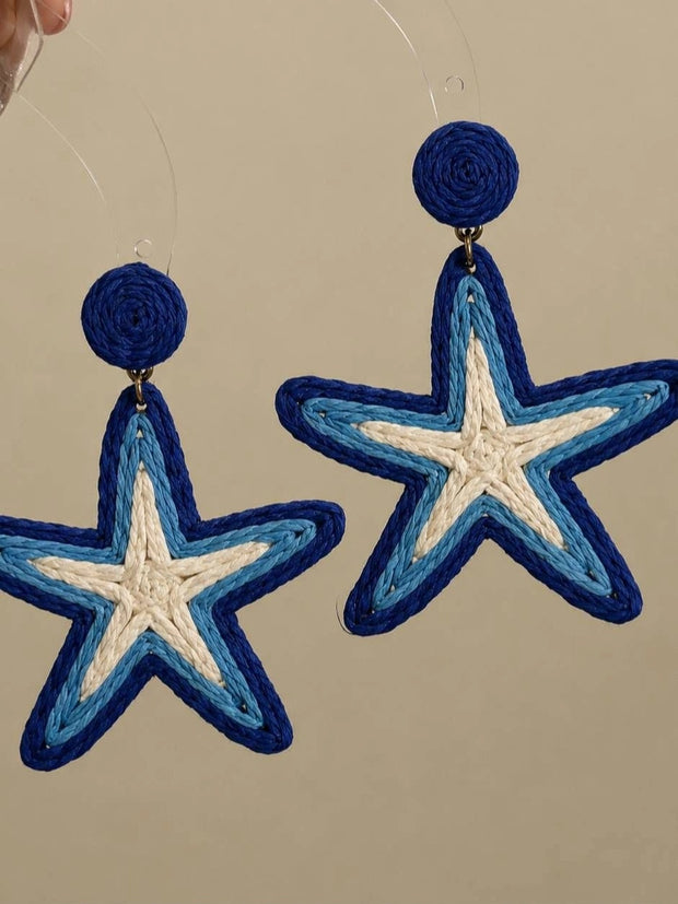 Pair of blue and cream raffia woven starfish drop earrings hanging against a neutral background