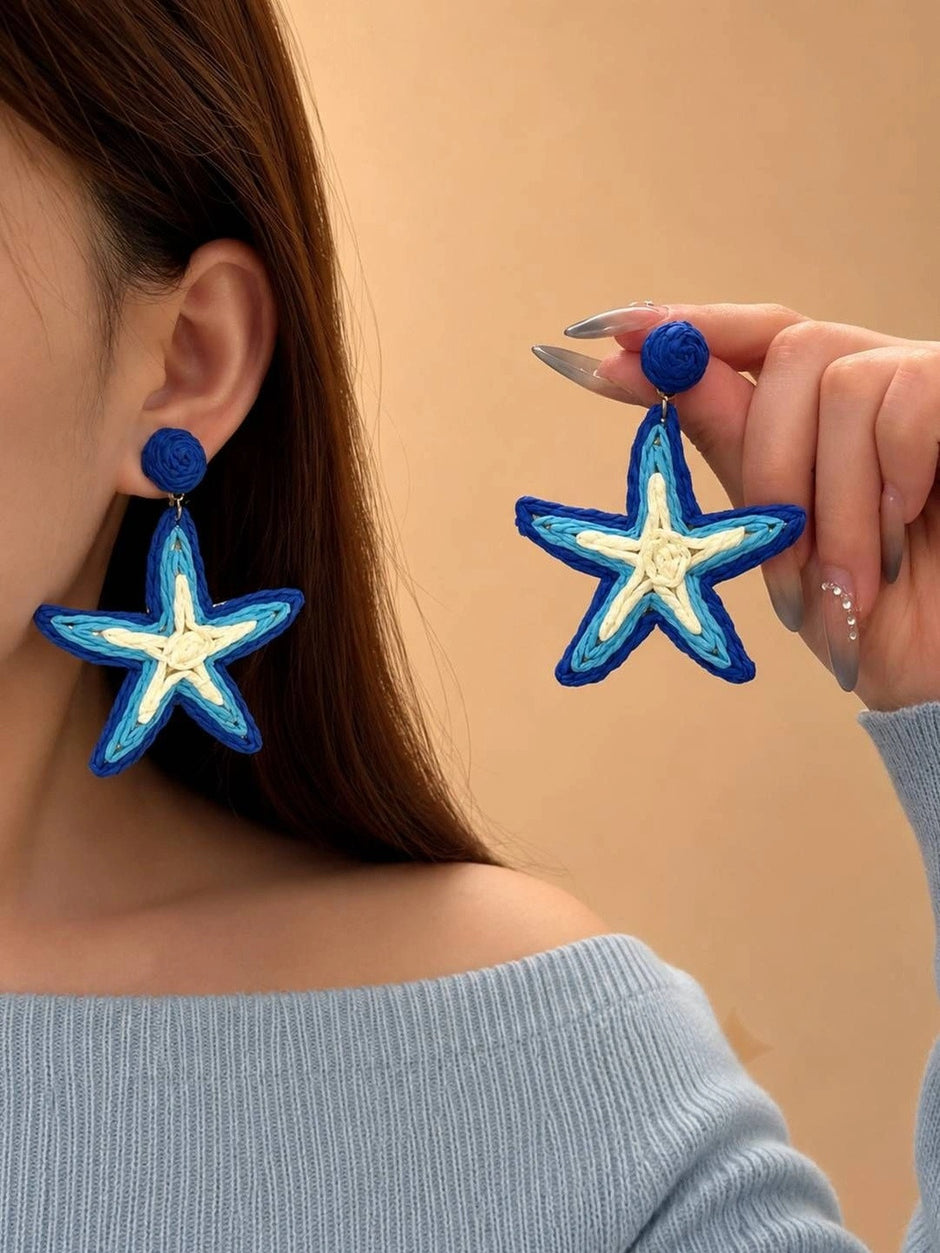 Woman wearing blue raffia starfish drop earring on one ear while holding the second earring up