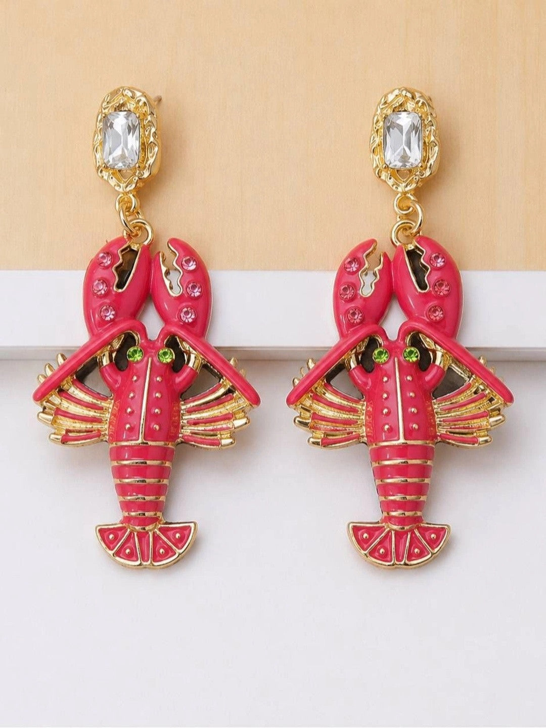 Pair of fuchsia enamel lobster drop earrings with gold-toned metal and rhinestone accents, flat lay on white surface