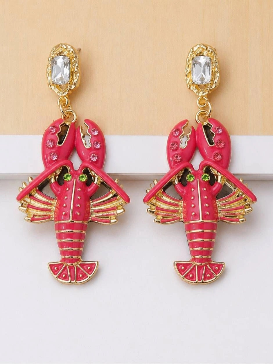Pair of fuchsia enamel lobster drop earrings with gold-toned metal and rhinestone accents, flat lay on white surface