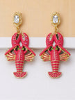Pair of fuchsia enamel lobster drop earrings with gold-toned metal and rhinestone accents, flat lay on white surface