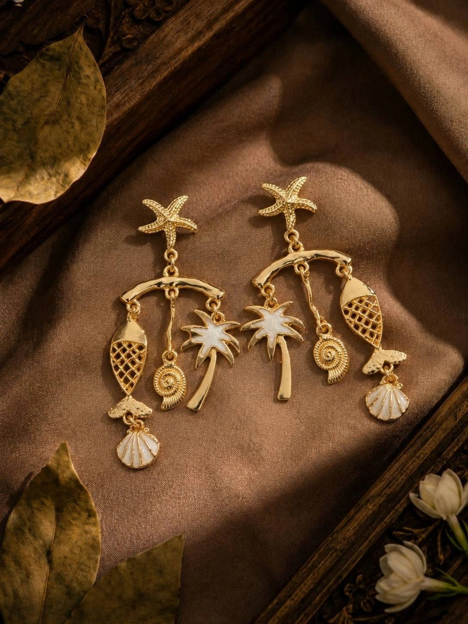 Pair of gold-plated coastal charm drop earrings with starfish studs, palm tree, fish and shell dangles on brown silk fabric