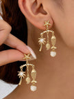 Close-up of gold coastal charm earrings worn on model's ear with starfish stud and dangling palm, fish and shell charms