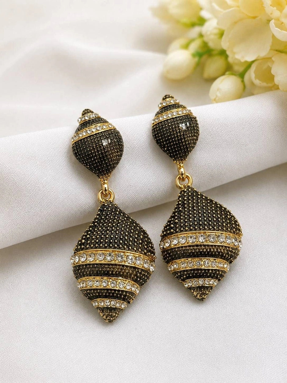 Close-up of both oxidised gold crystal spiral drop earrings on white fabric with flowers