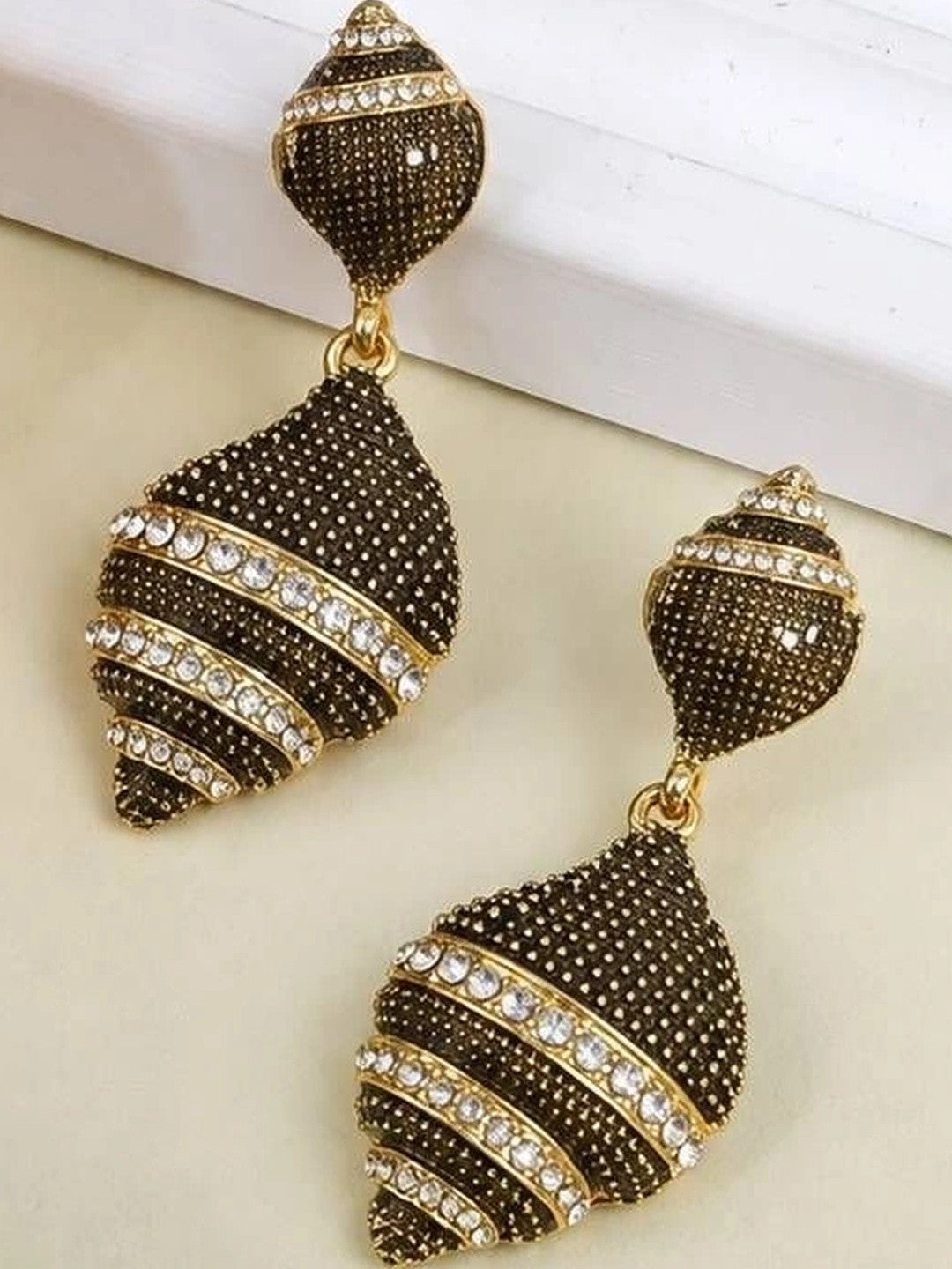 Two oxidised gold geometric drop earrings displayed apart on cream surface showing detail