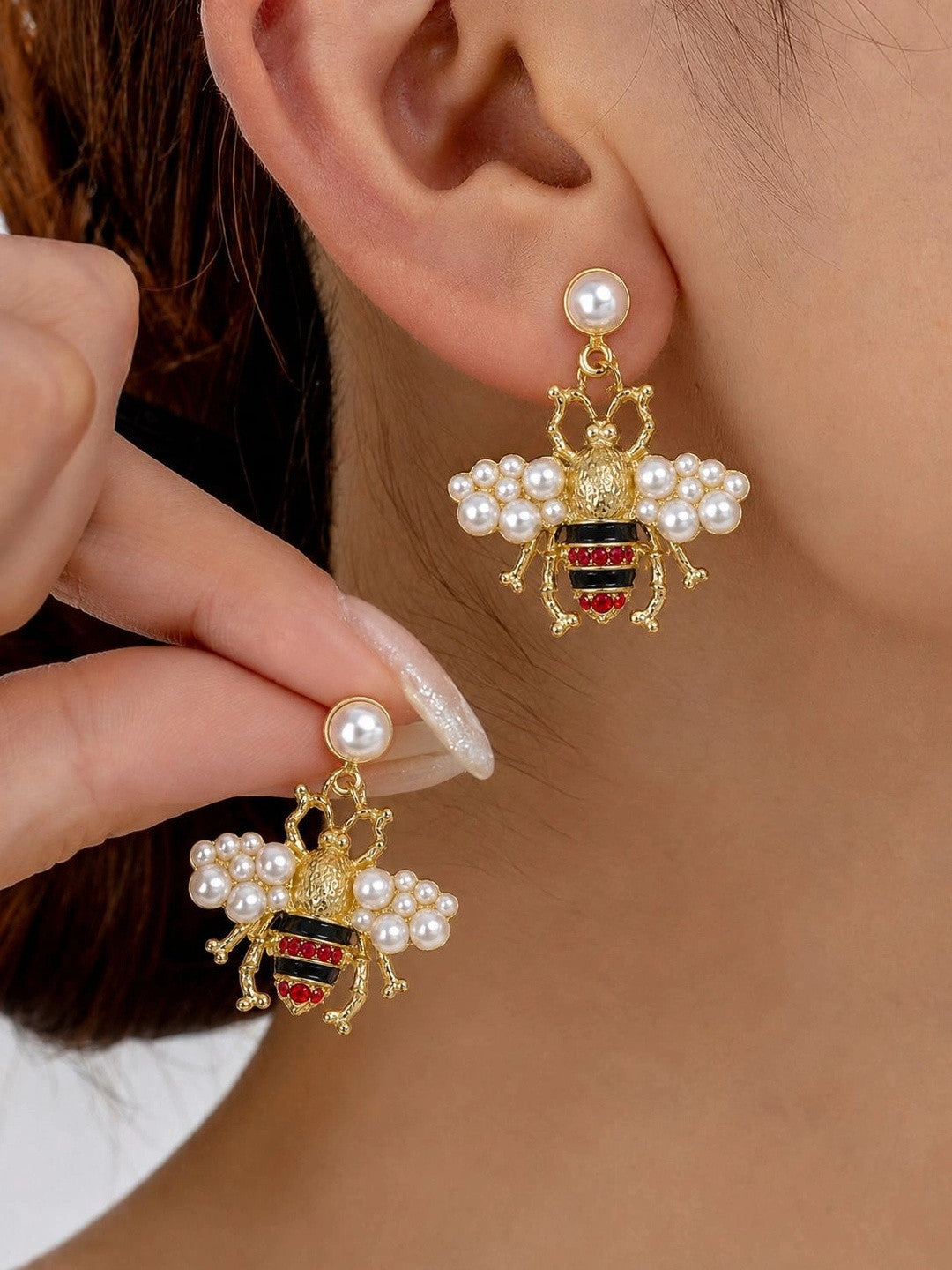 Gold-plated bee drop earring with pearl wings worn on ear, second earring held in hand showing front detail