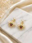 Two gold bee earrings with pearl-studded wings displayed on marble surface with dried white flowers