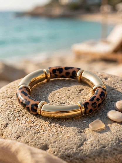 Gold-tone leopard print resin bangle resting on a sandy rock beside the sea