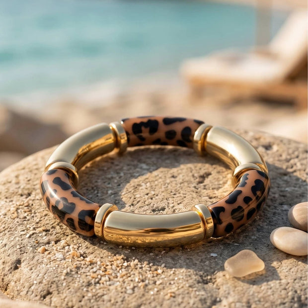 Gold-tone leopard print resin bangle resting on a sandy rock beside the sea