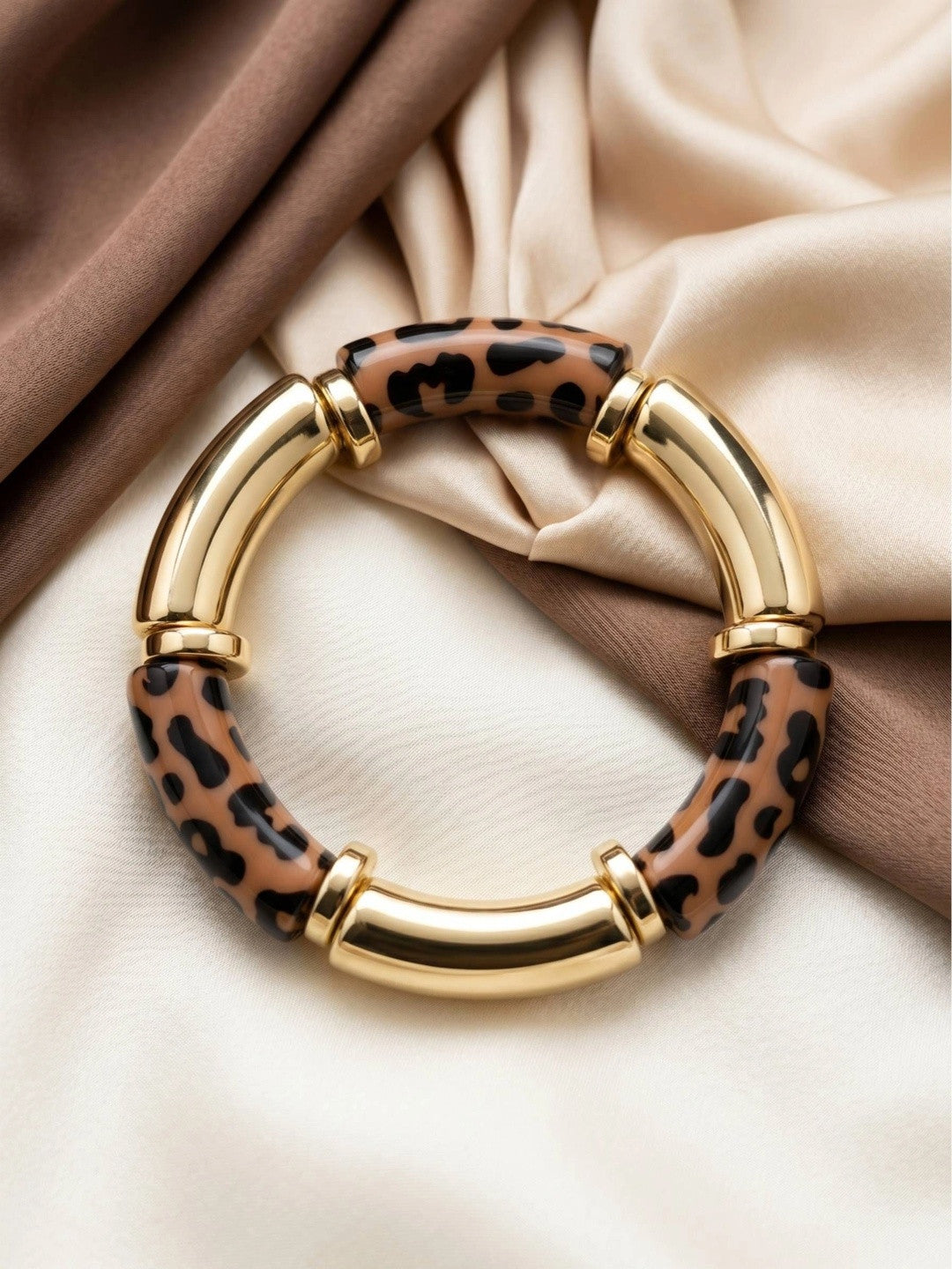 Leopard print and gold-finish resin bangle laid flat on ivory and brown silk fabric
