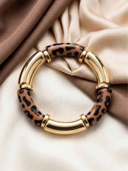 Leopard print and gold-finish resin bangle laid flat on ivory and brown silk fabric