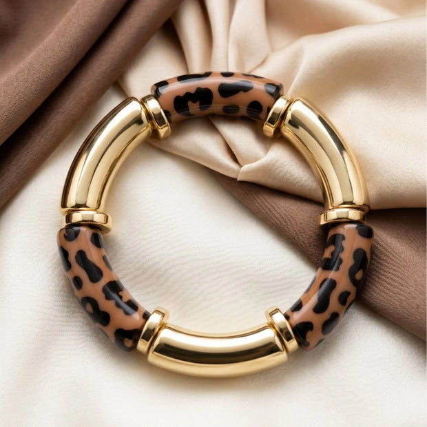 Leopard print and gold-finish resin bangle laid flat on ivory and brown silk fabric