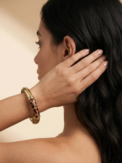 Woman wearing leopard print gold-tone bangle on wrist with hand raised to dark hair