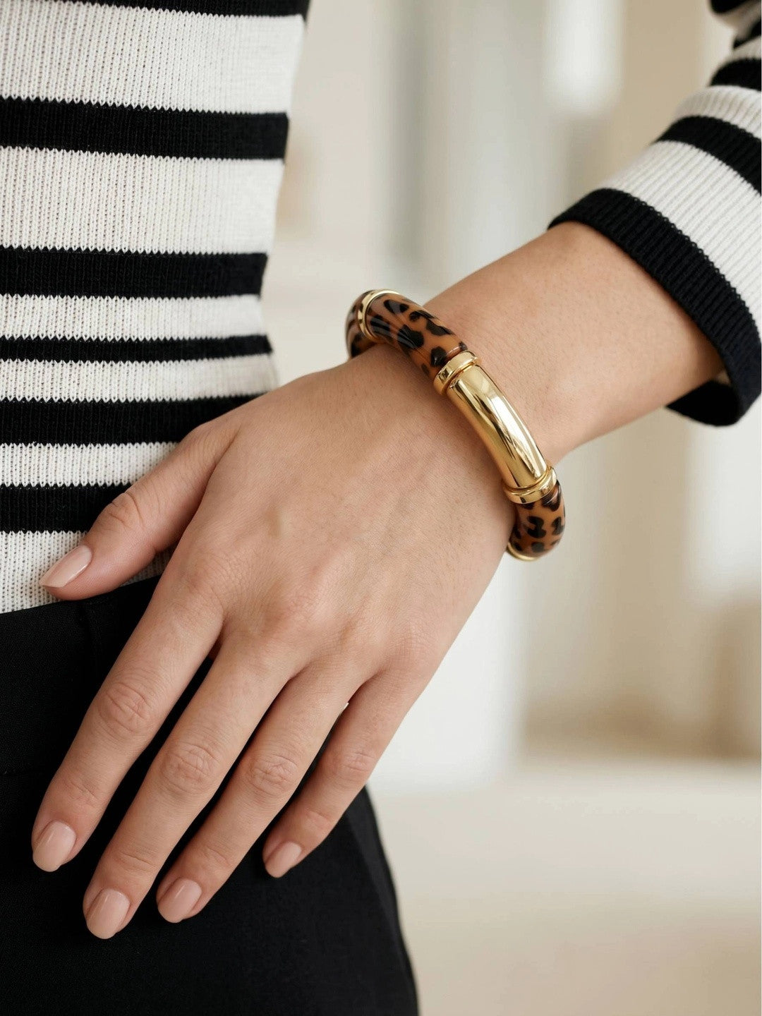 Close-up of leopard print resin bangle on wrist over black trousers and striped knit top