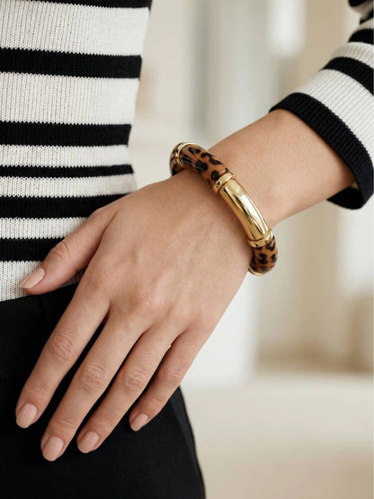Close-up of leopard print resin bangle on wrist over black trousers and striped knit top