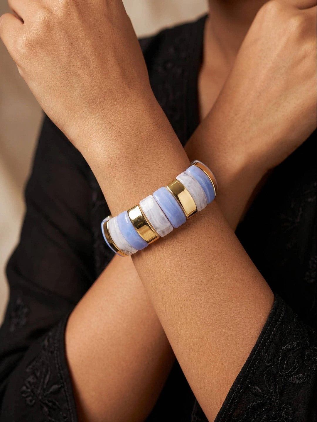 Blue and white striped resin cuff bangle worn on a woman's wrist against a black lace outfit with hands crossed
