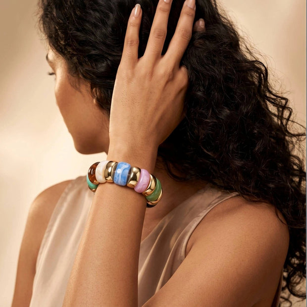 Woman wearing multicolour resin stretch bracelet on raised wrist against a warm beige studio background