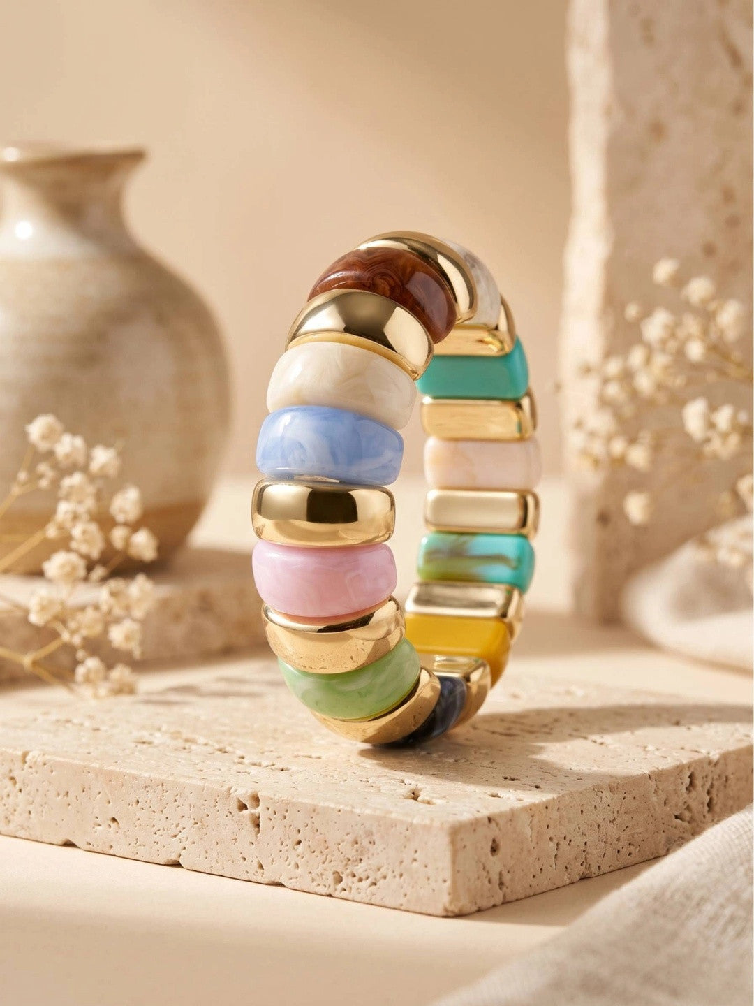 Multicolour resin stretch bracelet standing upright on a travertine tile with dried flowers in background