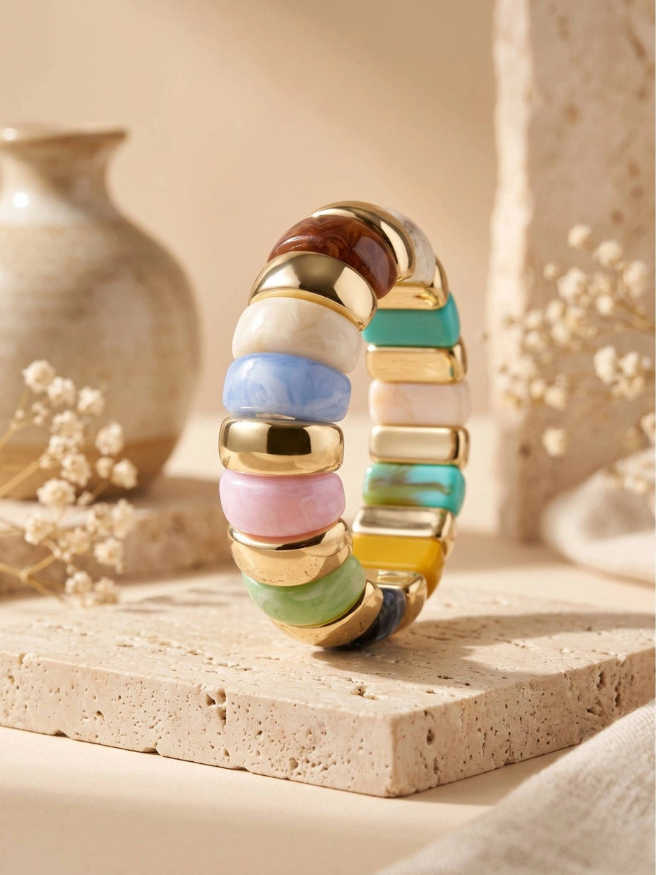 Multicolour resin stretch bracelet standing upright on a travertine tile with dried flowers in background