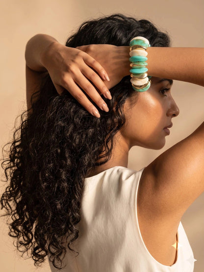 Woman with curly hair wearing turquoise marble resin cuff bracelet on her wrist raised behind her head