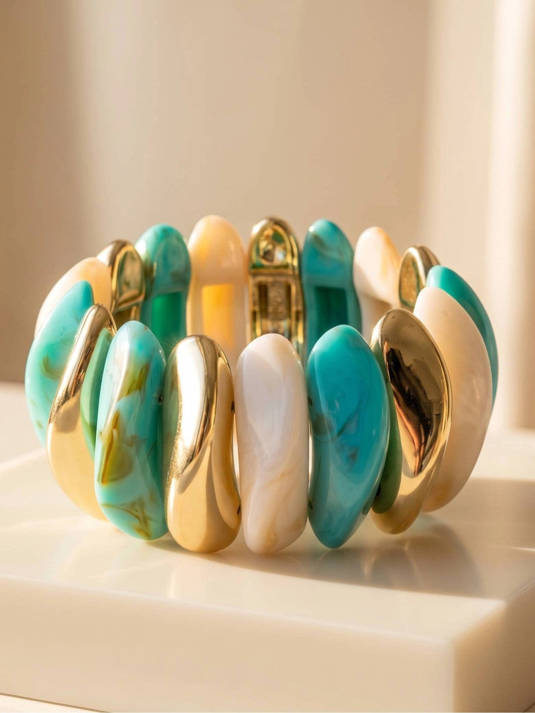 Turquoise ivory and gold-tone resin tile cuff bracelet standing upright on a white marble surface