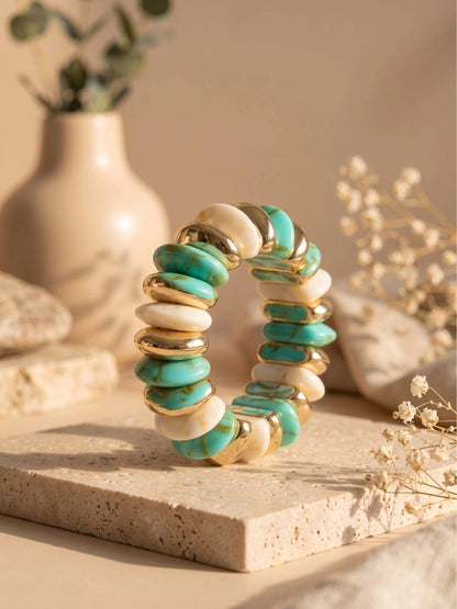 Turquoise marble resin bracelet standing on travertine tile surrounded by dried flowers and smooth stones