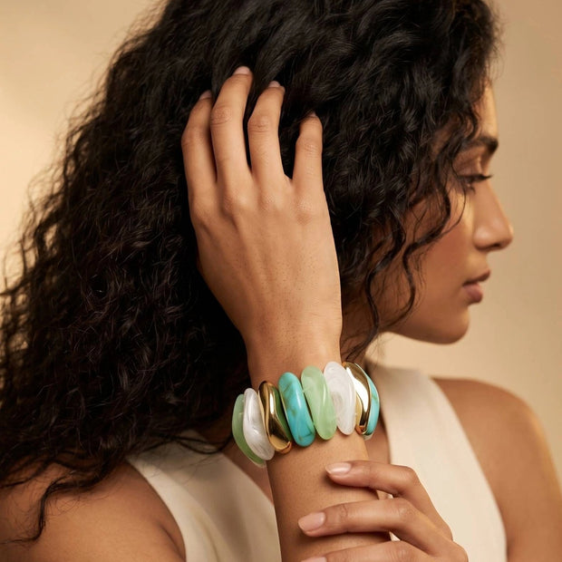 Model wearing resin stretch bracelet with multicolour links on her wrist against a warm beige studio background
