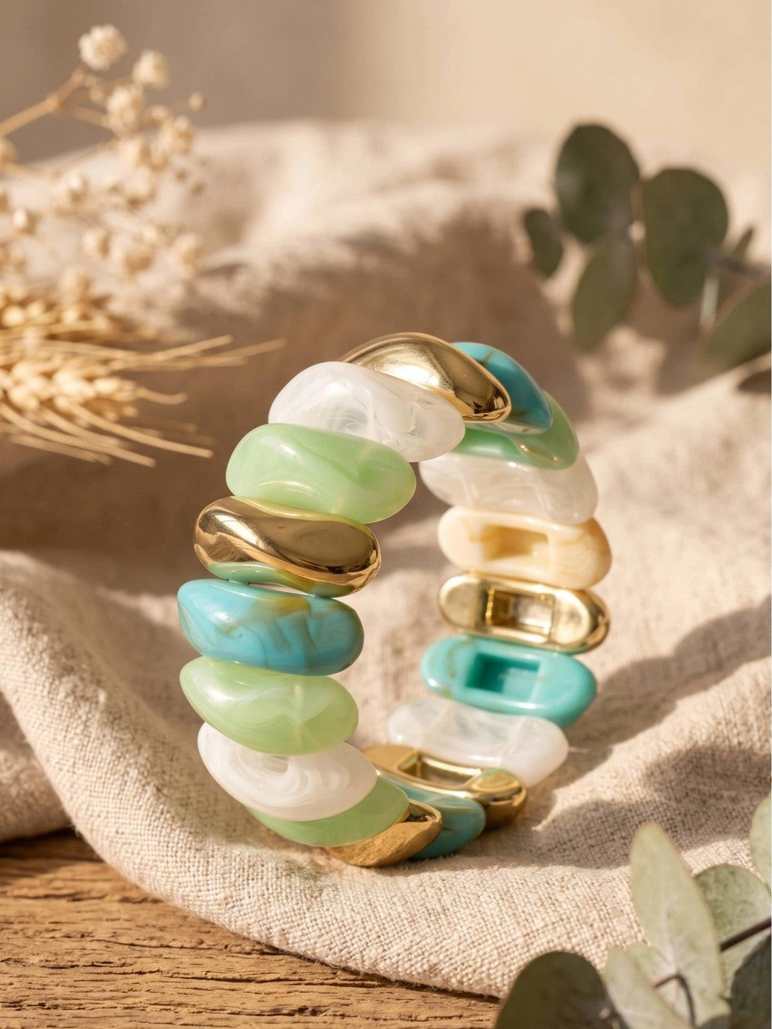 Resin stretch bracelet with mint, turquoise, white and gold links resting on cream linen fabric with dried eucalyptus