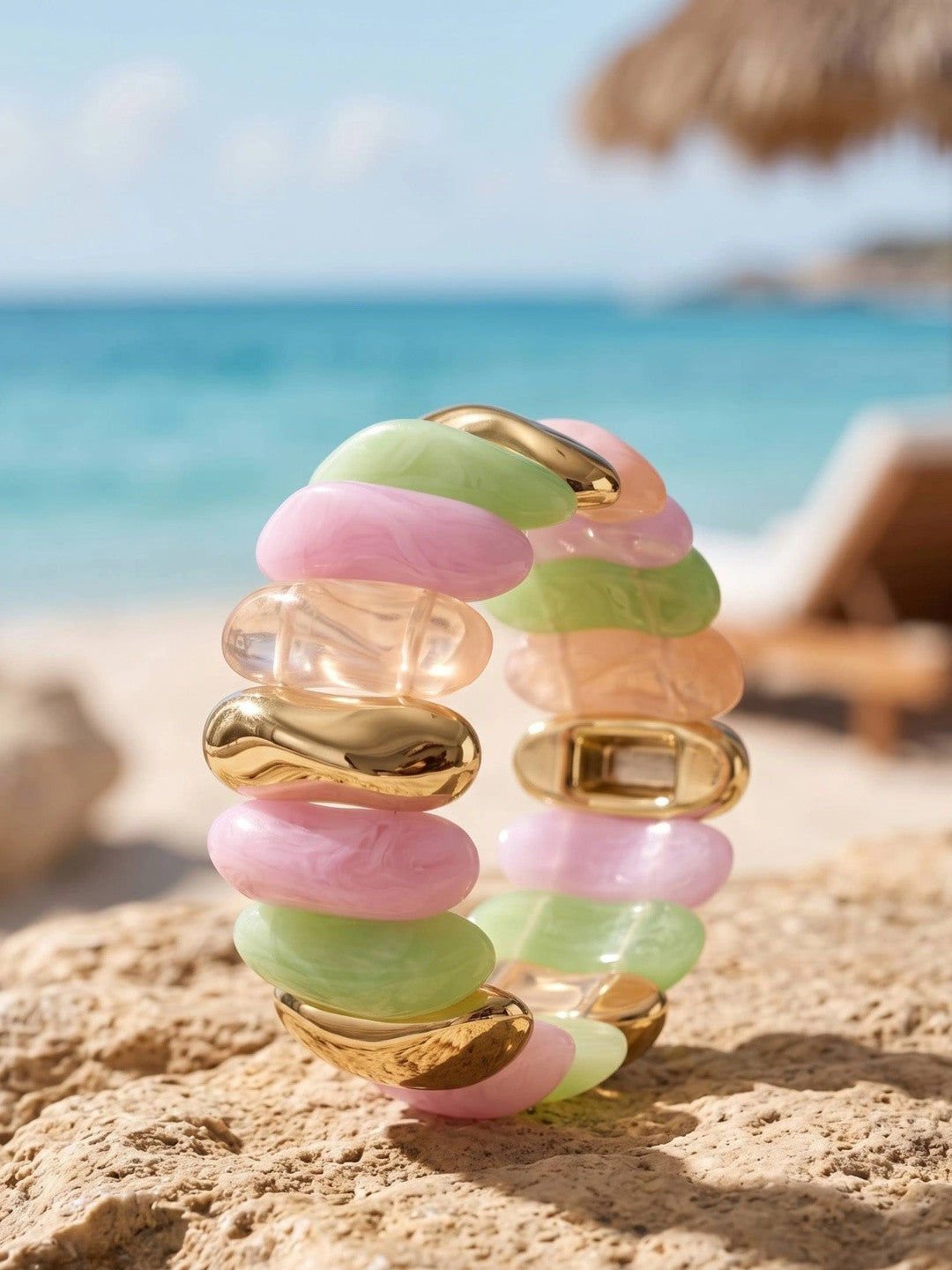 Pastel pink, mint green, peach and gold-tone stretch bracelet standing upright on sandy beach rock