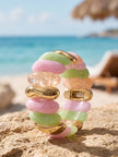 Pastel pink, mint green, peach and gold-tone stretch bracelet standing upright on sandy beach rock