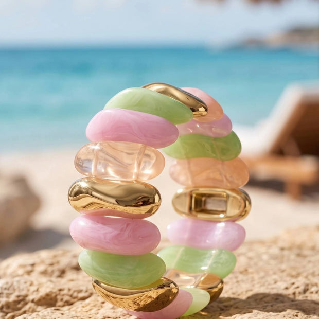 Pastel pink, mint green, peach and gold-tone stretch bracelet standing upright on sandy beach rock