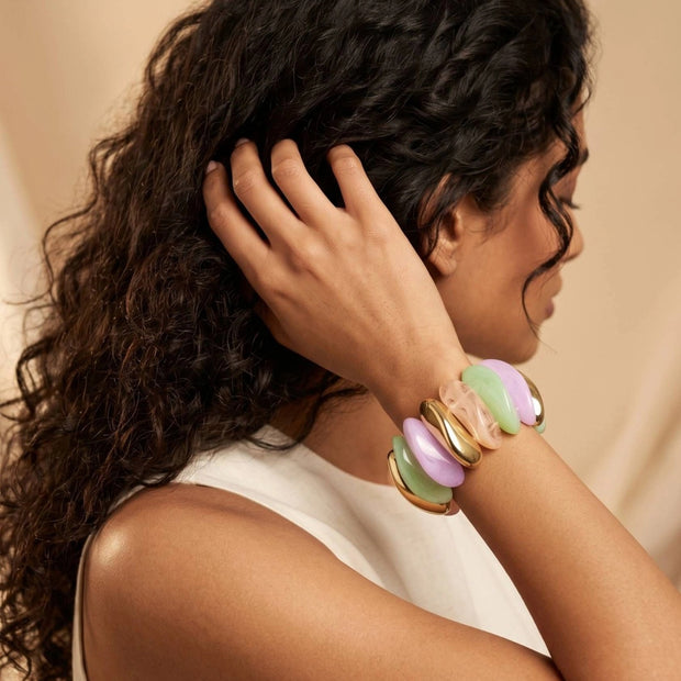 Woman wearing pastel resin and gold-tone stretch bracelet on wrist with hand raised to hair