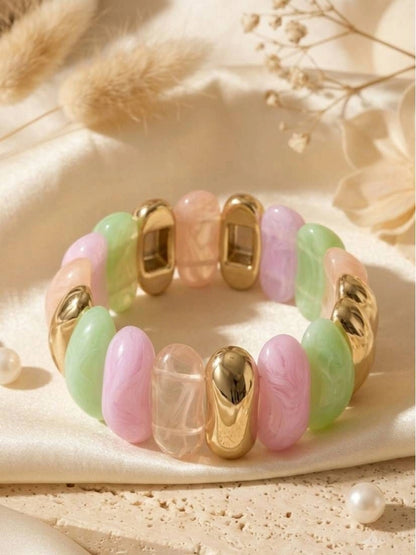 Flat lay of pastel resin stretch bracelet with pink, green and gold-tone beads on cream silk fabric