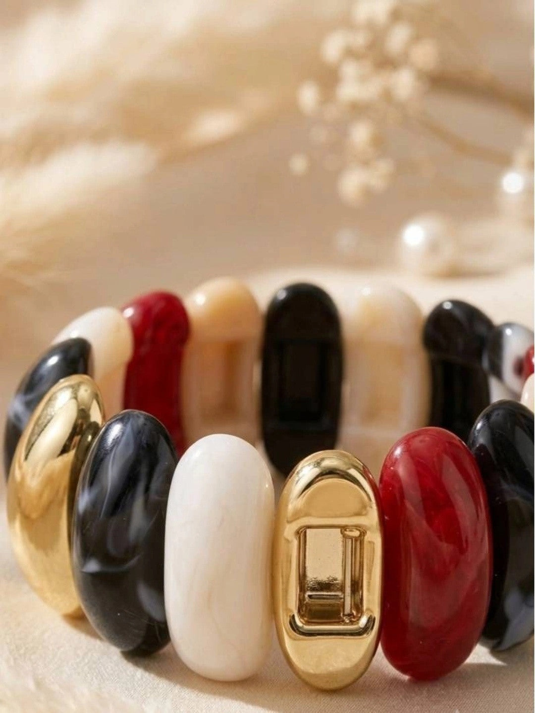 Close-up of multicolour resin cuff bracelet showing gold-toned clasp and glossy red, black, white, and marbled oval segments